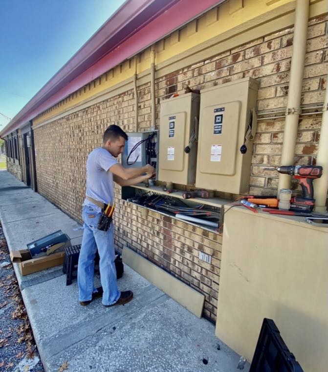 Electrician wiring twin service panels on a commercial brick exterior